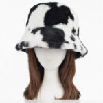 A plush faux fur bucket hat featuring a bold cow print pattern, available in both classic black-and-white and warm beige-and-white.