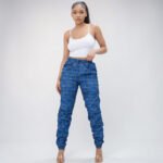 A model wearing skinny-fit windbreaker joggers featuring a classic plaid print in vibrant royal blue. The joggers showcase a comfortable drawstring waist, a lightweight structural fabric, and stylish shirred ankle cuffs.