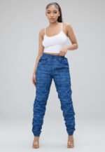 A model wearing skinny-fit windbreaker joggers featuring a classic plaid print in vibrant royal blue. The joggers showcase a comfortable drawstring waist, a lightweight structural fabric, and stylish shirred ankle cuffs.