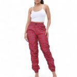 A model wears high-waist, skinny-fit red plaid windbreaker joggers. The pants have a drawstring waist and shirring details at the ankles, which creates a jogger silhouette.