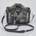 Small black vegan leather handbag shaped like a moto jacket, featuring silver metal studs, decorative zippers, and a structured clutch silhouette.