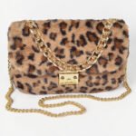 Close-up of a luxurious faux fur shoulder bag in a classic tan and black leopard print, featuring a structured crescent shape and polished mixed-metal hardware.